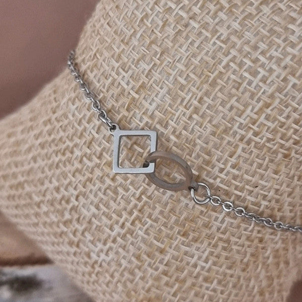 Bracelet argenté minimaliste en acier inoxydable porté au poignet avec losange et cercle entrelacés