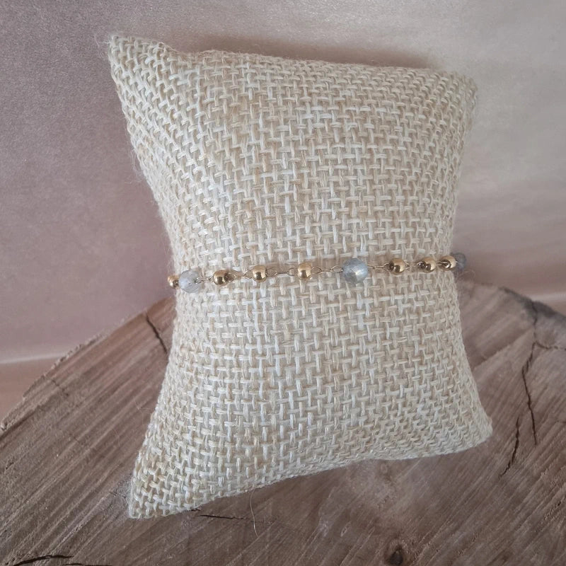 Bracelet doré avec perles blanches vue de face sur coussin en toile.