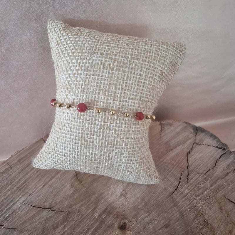 Bracelet doré avec perles roses vue de face sur coussin en toile.
