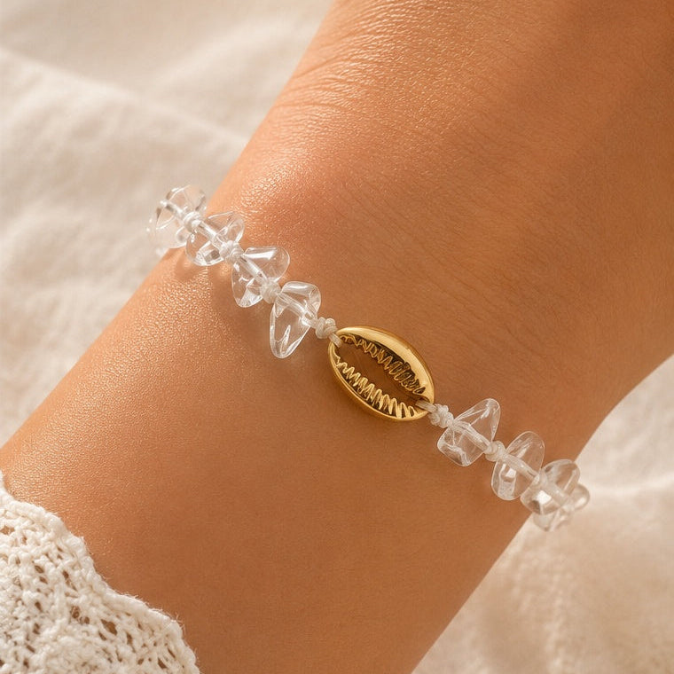 Bracelet femme à cordon blanc orné de pierres transparentes et d'un coquillage doré, esprit bord de mer.