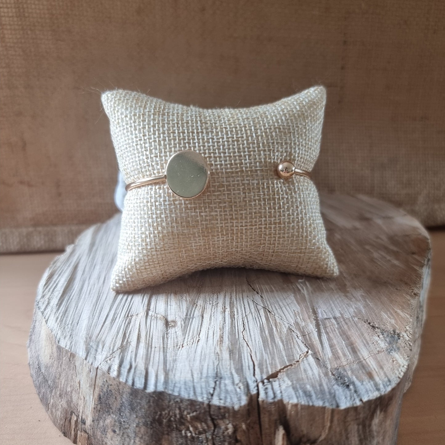 Bracelet doré fin avec médaillon rond présenté sur coussin en toile