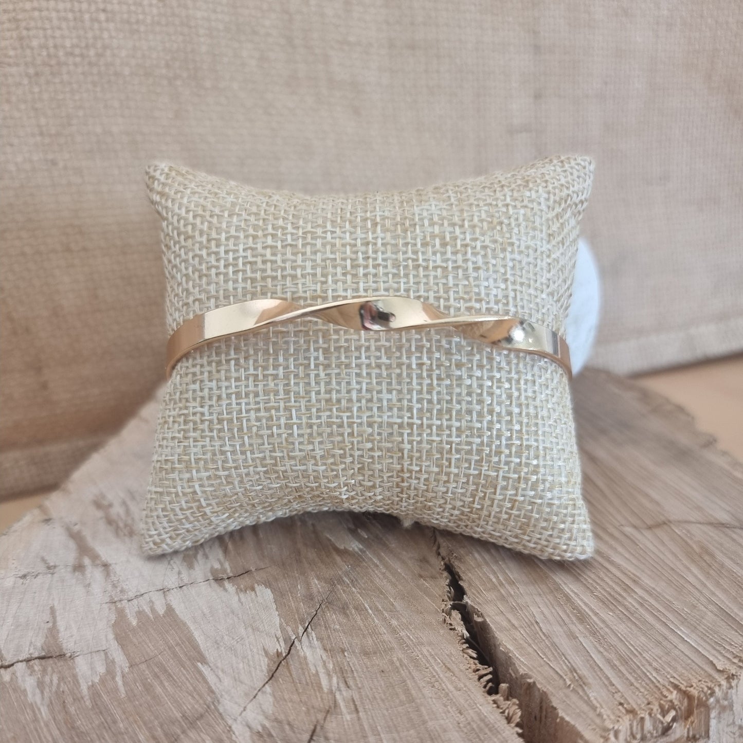 Bracelet jonc doré torsadé posé sur support en bois