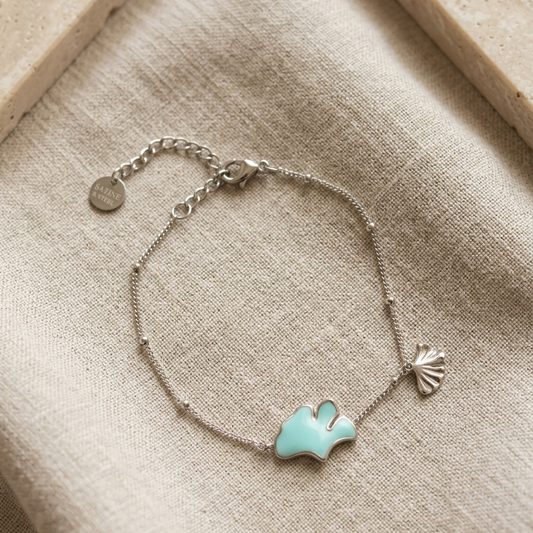 Bracelet en acier inoxydable doré orné d'un charm en forme de coquillage et d'un pendant en forme de feuille de Ginkgo biloba émaillé de bleu turquoise.