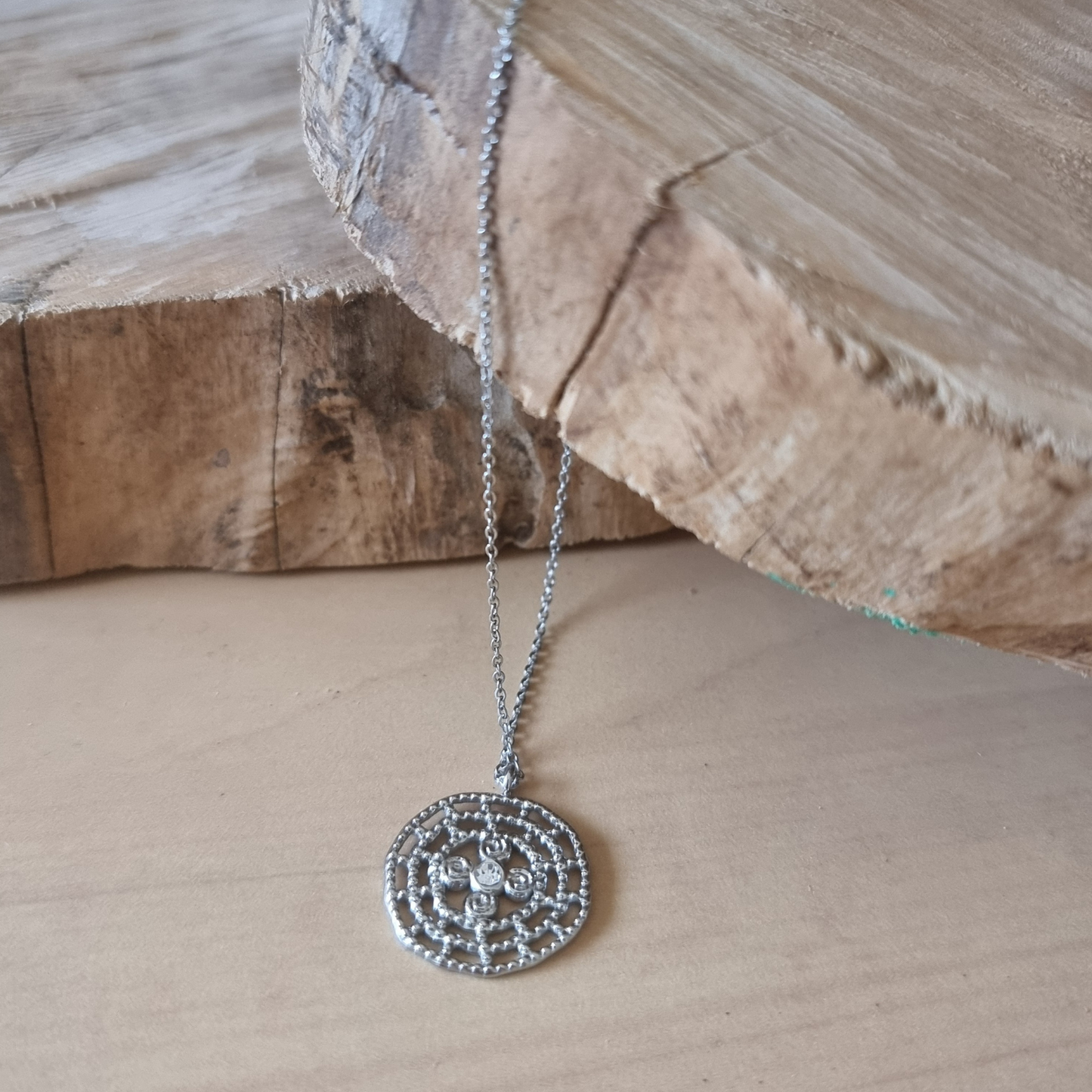 Gros plan sur le pendentif rond ajouré argenté.