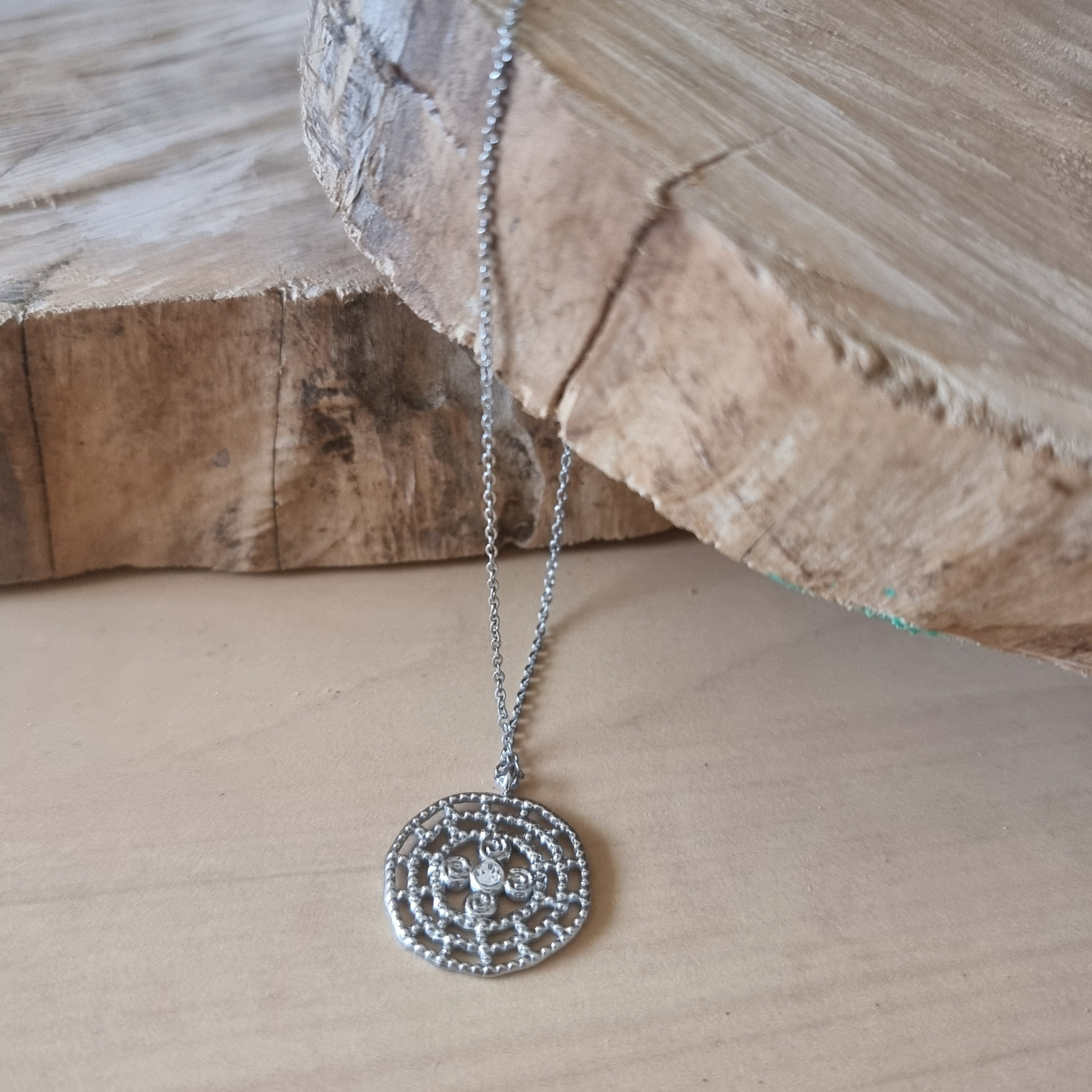 Gros plan sur le pendentif rond ajouré argenté.