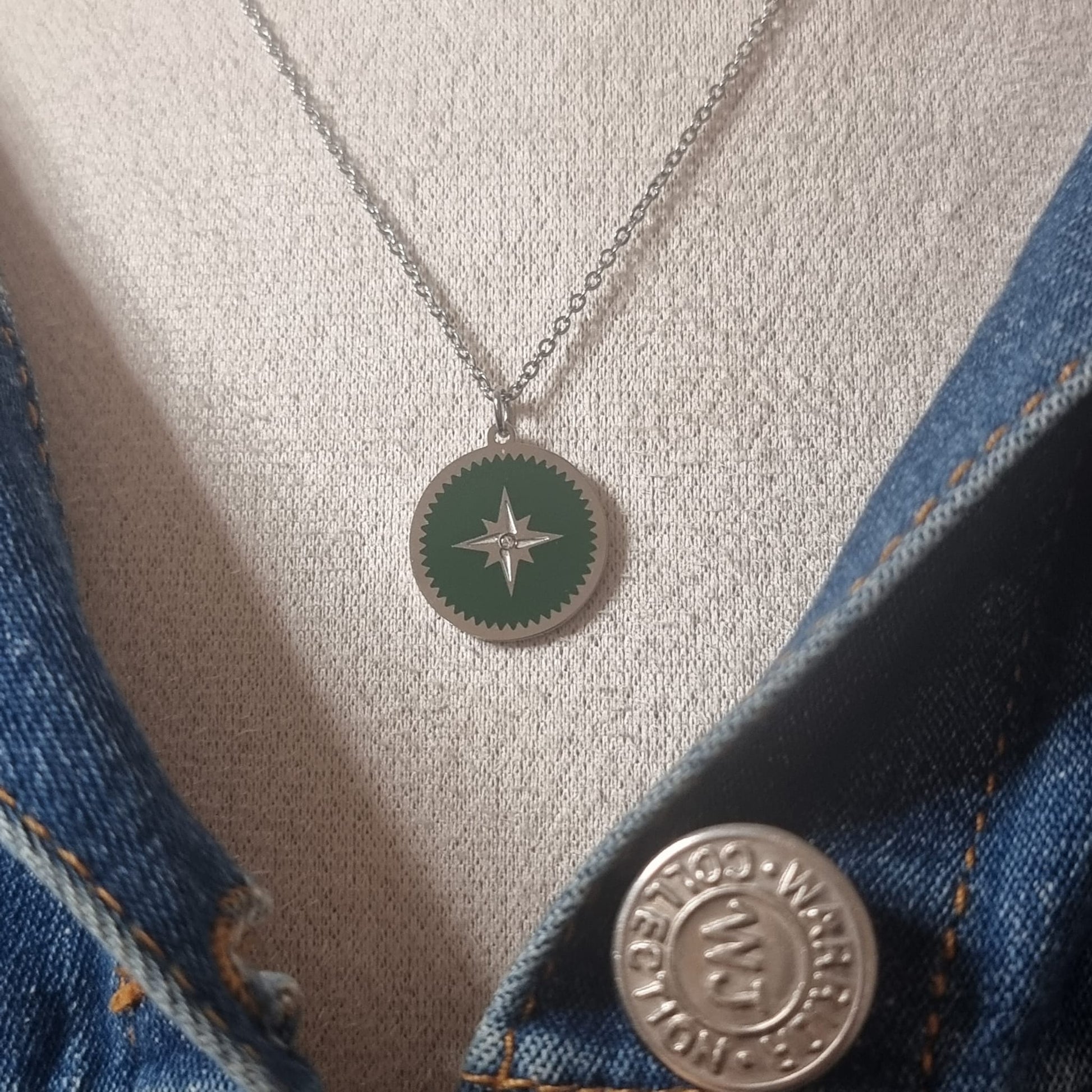Pendentif rond vert et argent porté sur une veste en jean's.